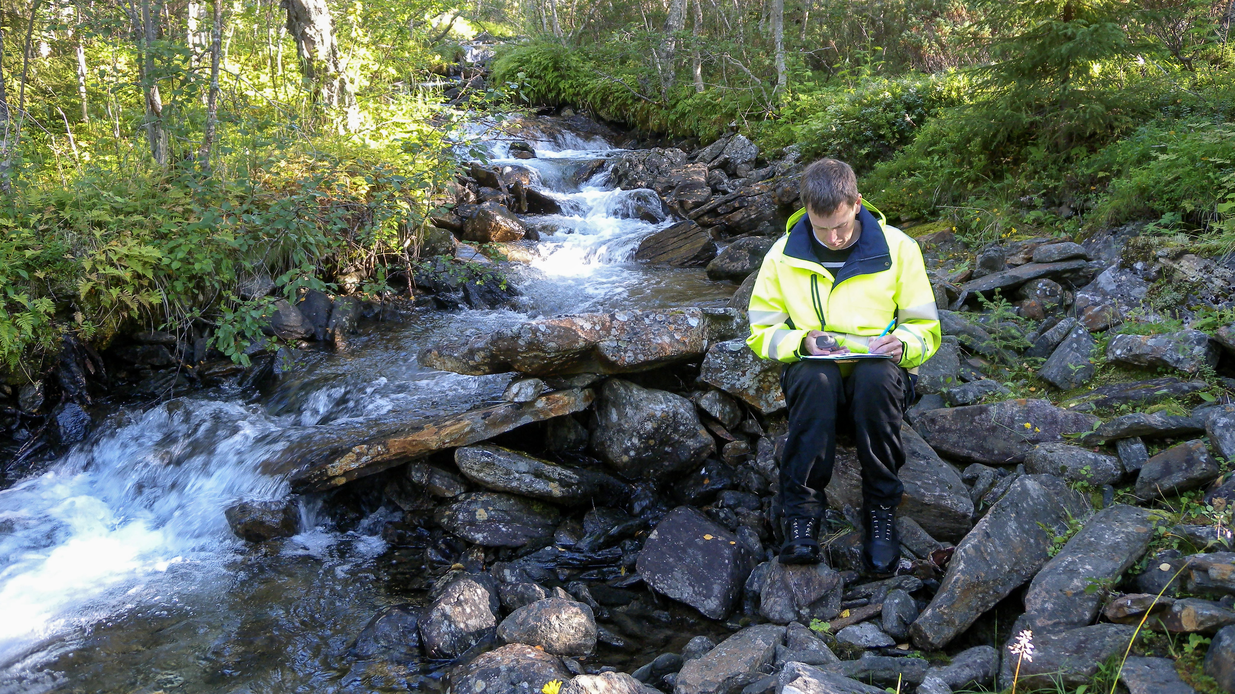 En man står på stenar intill en bäck.