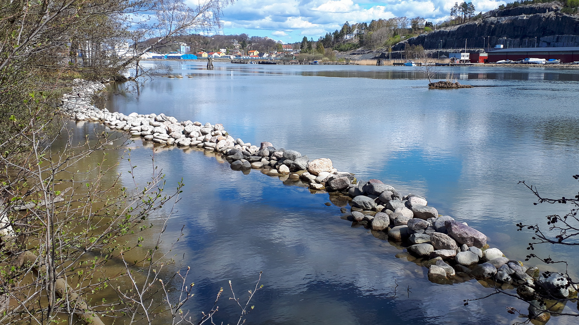 En flod med stenar på sidan och en bro i bakgrunden.