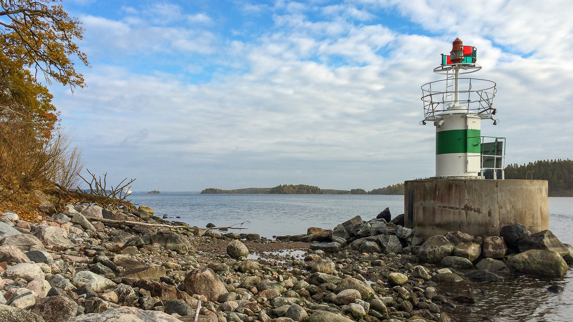 En grön och vit fyr som sitter på toppen av en klippig strand.