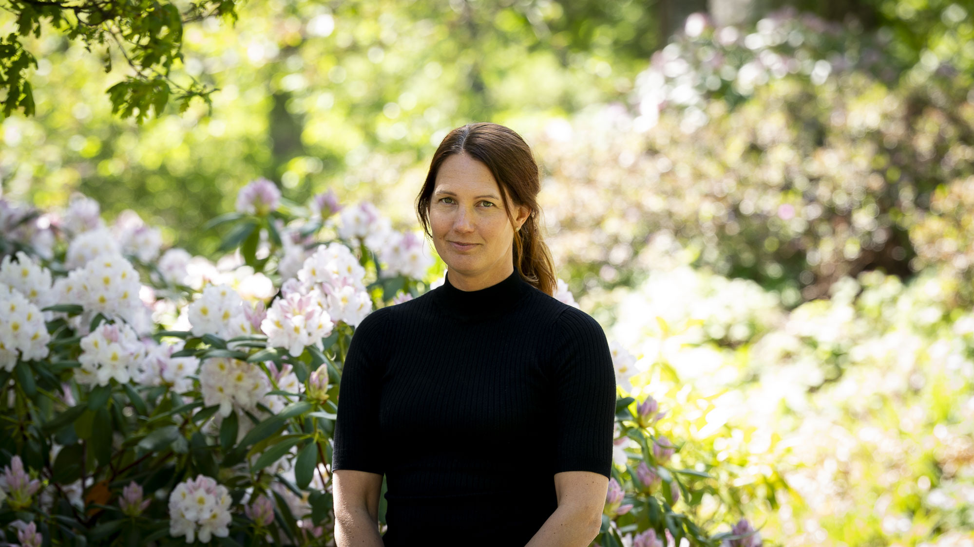 En kvinna står framför en buske med blommor.